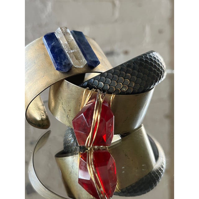 A thick brushed gold-plated statement brass cuff with a wired red resin stone at center. The resin is faceted to mimic a...