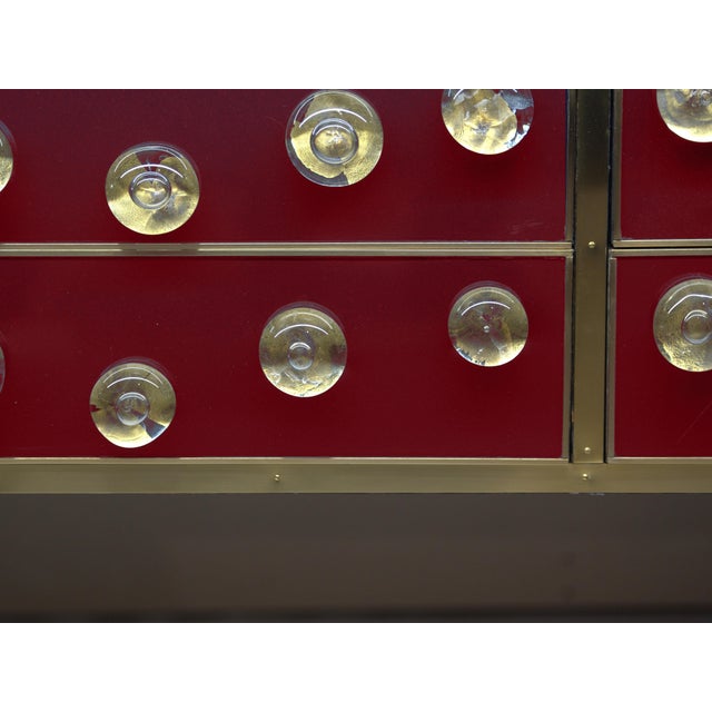 Italian burgundy sideboard with a birch-wood structure, brass framing and 28 circular Murano glass accents. Its...