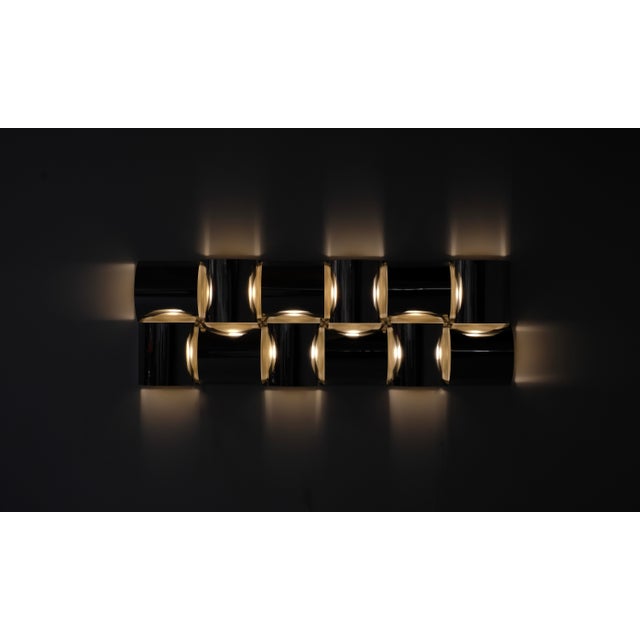 Wall light composed of four polished stainless steel panels mounted on a white metal frame, with a fiberglass diffuser....