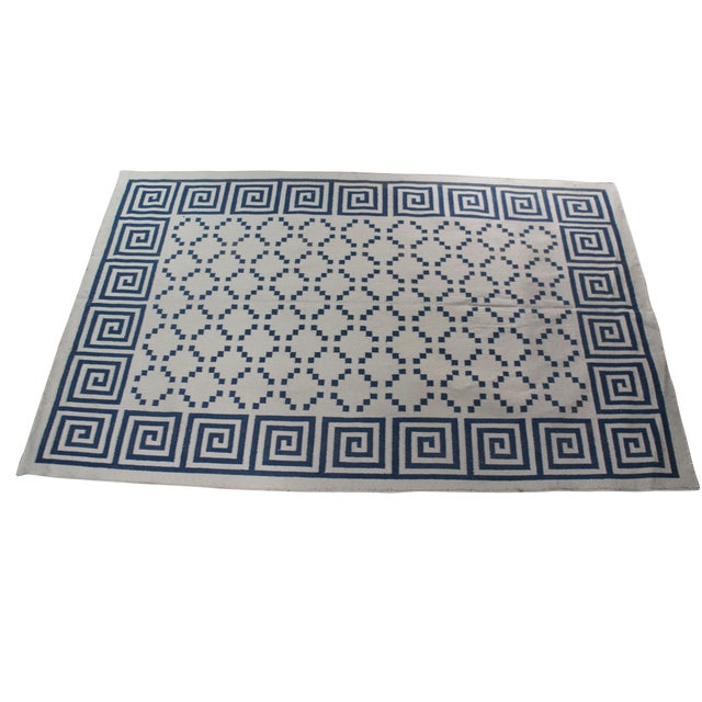 A handwoven cotton Greek key dhurrie rug. It features a classic meander border motif paired with a central lattice grid...