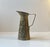 A decorative pitcher in light brass embossed with a medieval pub scene all around its perimeter. Manufactured in England...