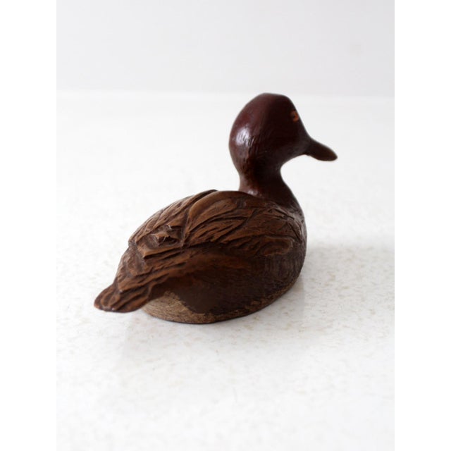This vintage hand-carved wooden duck figurine features intricate carved details and glass eyes. The craftsmanship is...