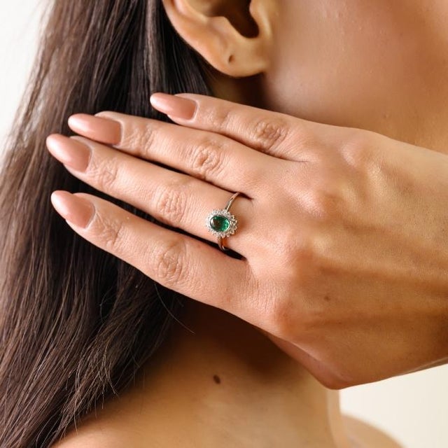 This elegant halo engagement ring features 1 natural oval-cut zambian emerald totaling 0.49 carats, set in 14k white gold....