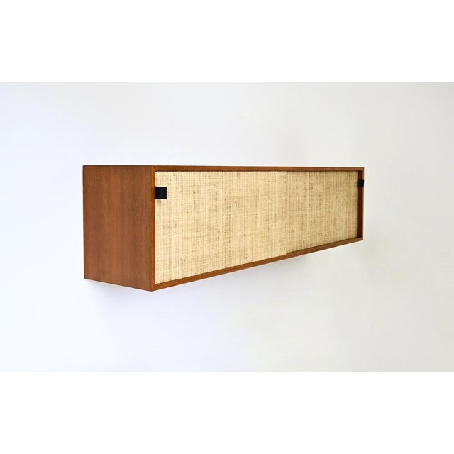 A two-door sliding sideboard by Florence Knoll, lined with canvas and featuring leather handles, designed to be hung on...