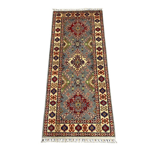 This Kazak-style wool runner has a gray field with three bold tribal medallions. A cream border frames the design, while...