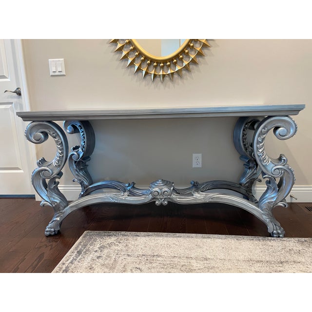 Stylish contemporary console made by Oly Studio with a romantic ornately hand-carved grey painted base with intricate...