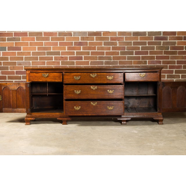 An English oak long buffet from the 19th century with five drawers, two doors, brass hardware and carved feet. Step back...