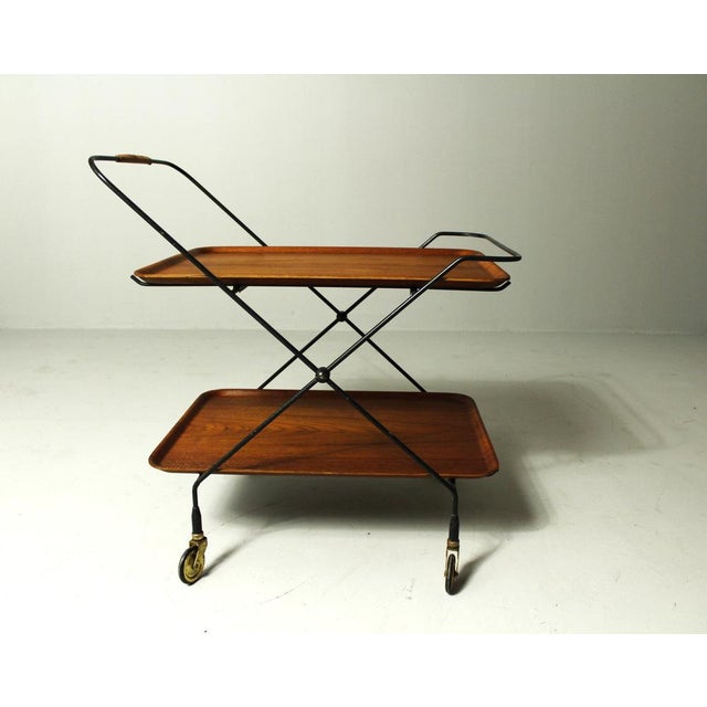 Folding metal wire rack on brass rolls with inserted teak woodtrays. It is in very good condition with beautiful patina....