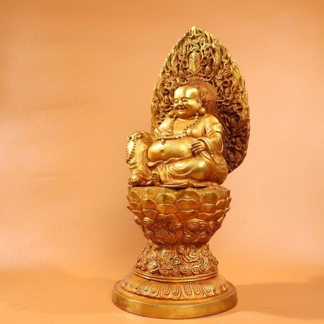 A beautiful gilded bronze sculpture of the Laughing Buddha seated on an ornate lotus pedestal with elaborate carved...