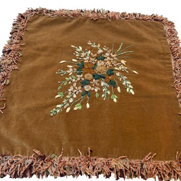 A charming vintage cushion cover featuring an embroidered floral bouquet on a soft light brown velvet ground. The bouquet...