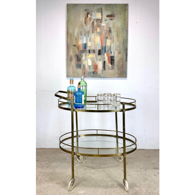 A beautiful and well-made two-tier bar cart with solid brass frame, clear glass shelves and clear plastic casters, circa...