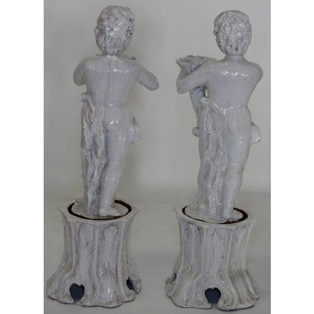 This is an elegant pair of 19th century white crackle glazed terracotta cherub statues. Gracefully displayed atop tree...