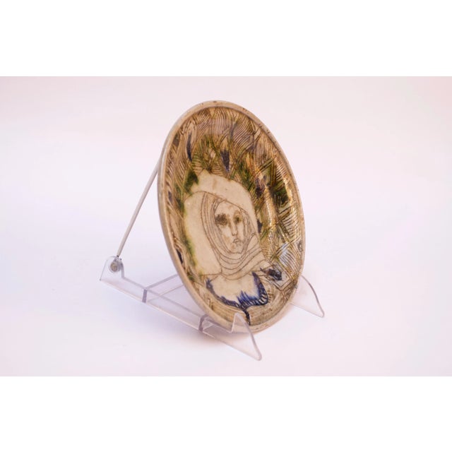 Studio ceramic decorative plate depicting a woman with a headscarf. Linear and geometric details present along with pops...