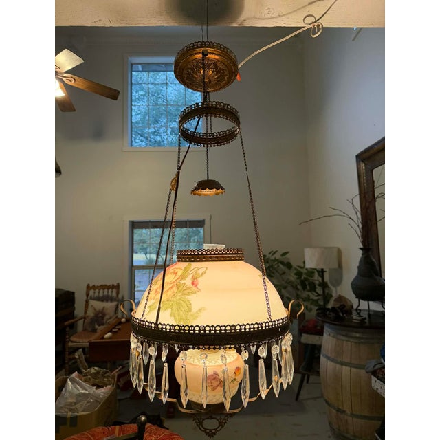 This elegant antique hanging chandelier features a hand-painted milk glass dome shade adorned with soft floral motifs in...