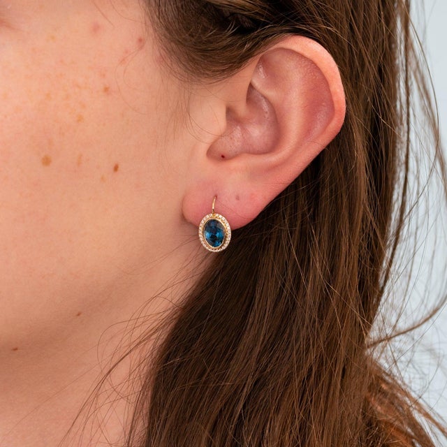 Deep London blue topaz gemstones shimmer within a halo of diamonds in these oval studs, crafted in solid 14K yellow gold....