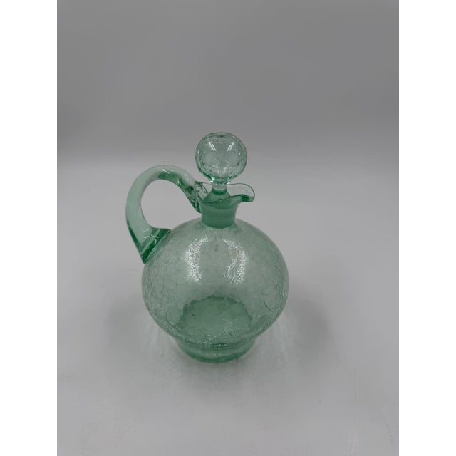 Glass decanter in a greenish hue with a clearly visible crackle/broken glass effect and a matching ball stopper. The glass...