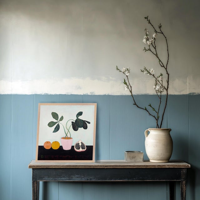 A brightly colored still life with orange fruit, a potted plant, and a pomegranate. Framed in an FSC Certified wood frame...