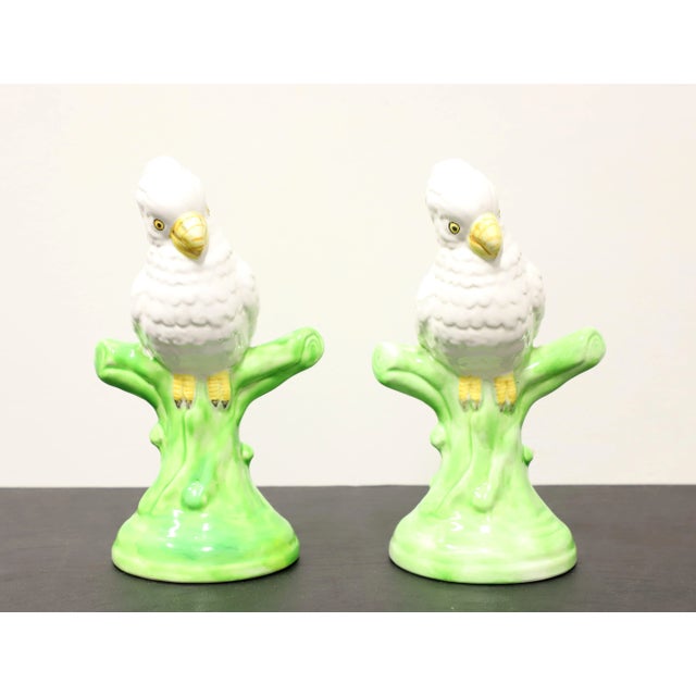 A pair of porcelain figurines depicting white parrots on tree branches. Multi-colored porcelain of primarily white, green,...