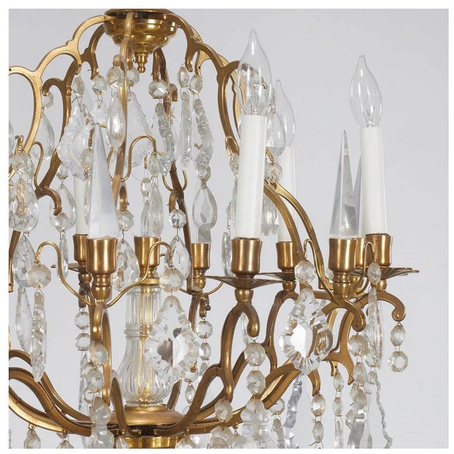 An elegant twelve arm chandelier featuring a gilt brass frame richly draped with faceted crystal pendants and drops. The...