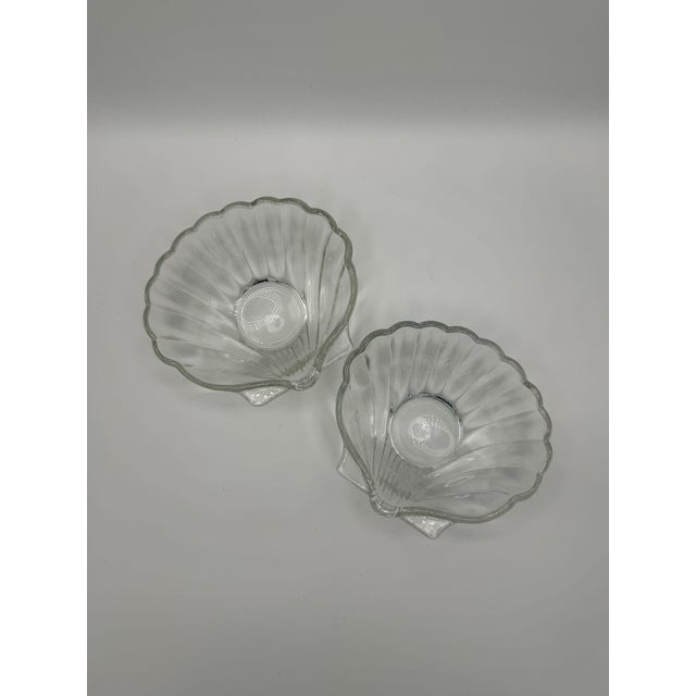 A pair of vintage clear glass scallop seashell dishes or trinket bowl with a ribbed texture and small resting feet.