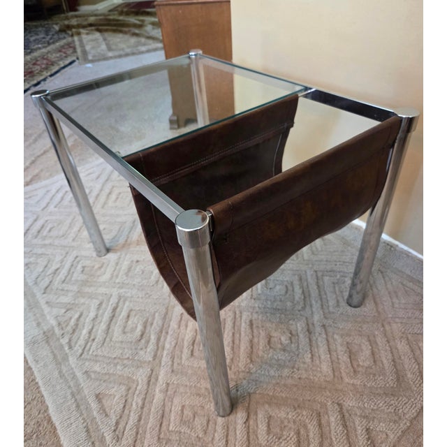 In the style of Mile Baughman. Chrome and glass table with leather magazine/document holder.