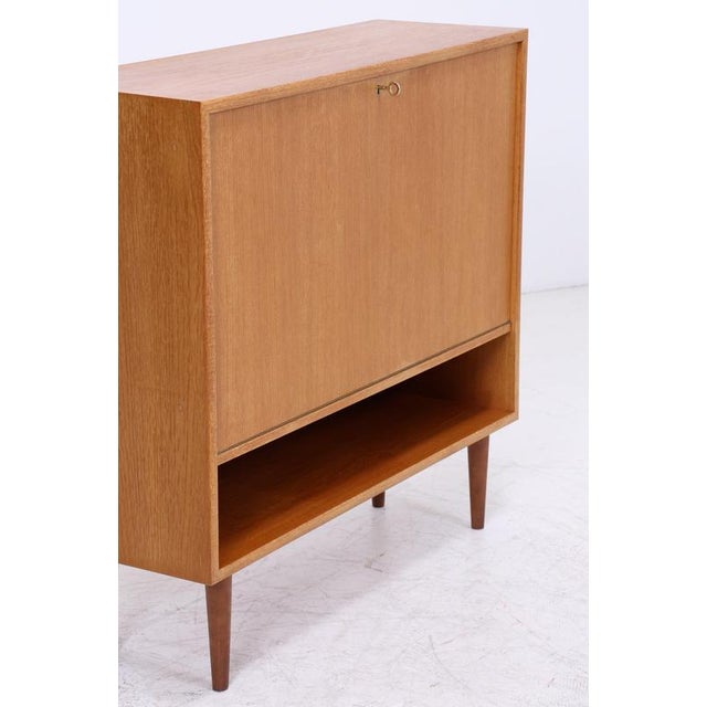 Vintage bar cabinet from the 1960s with a well-designed interior. Behind the flap are a mirror, a glass shelf, and a...