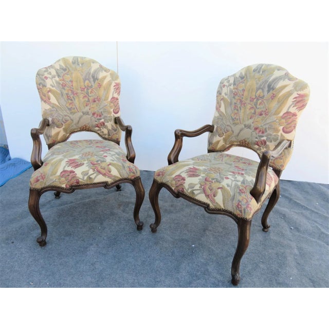 A pair of Louis xv style open arm chairs, Walnut frames with floral tapestry upholstery, cabriole legs with brass nail...