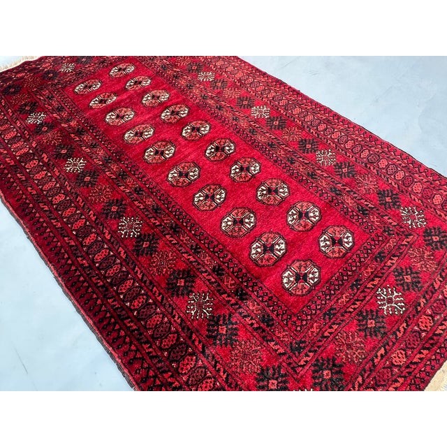 A richly saturated vintage Afghan Mauri Bokhara rug — a single central column of large, rounded oval Tekke guls runs the...