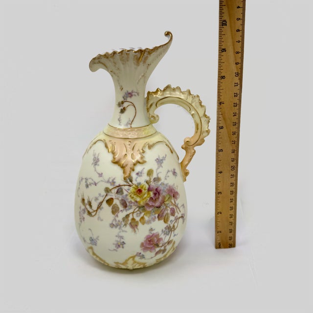 An elegant antique porcelain ewer-style vase featuring delicate hand-painted floral motifs with soft pink, yellow, and...