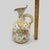 An elegant antique porcelain ewer-style vase featuring delicate hand-painted floral motifs with soft pink, yellow, and...