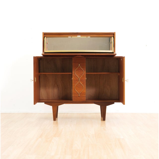 This fabulous mid century bar cabinet was made in England during the 1960s. Produced in teak, the top cabinet doors open...