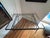 Features a striking geometric Greek-key style inner apron, splayed legs, and an inset thick flat-polished floating glass...
