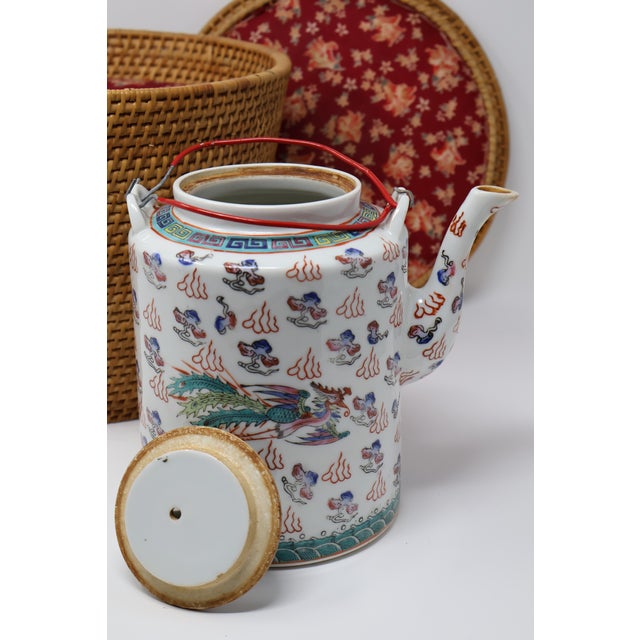 A colorful Chinese porcelain teapot paired with a fitted woven warming basket, bringing together intricate decoration and...