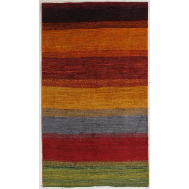 Hand-knotted Persian Gabbeh wool rug featuring broad horizontal bands in rich tones of red, gold, rust, gray, and green....