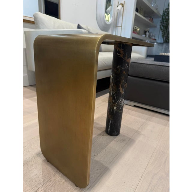 A sensuous ribbon of L-shaped light antique brass-finished steel is supported by an impressive Michelangelo marble...