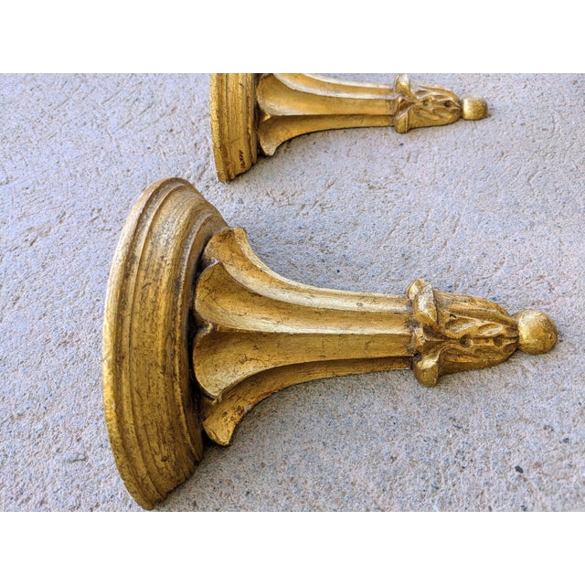 Beautiful pair of hollywood regency, gold giltwood, gold-leaf, corbel style shelves. These bracketed shelves feature a...