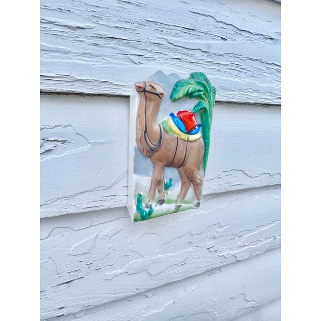 Whimsical vintage Japanese porcelain wall pocket, modeled as a camel carrying colorful packs and backed by stylized palm...