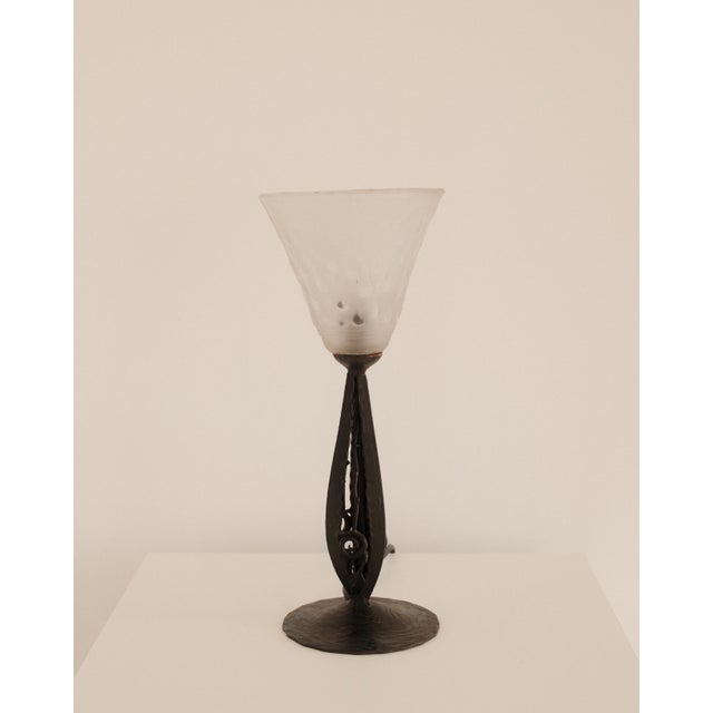 An openwork metal stem gives the lamp its slender architectural poise, with the glass shade completing the form in a...