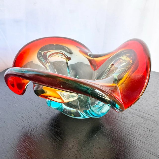 A striking mid-century Murano-style art glass dish featuring vivid swirls of red, amber, and aqua blue. Hand-blown with...