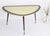 A large kidney shaped glass formica table with a brass rim standing on wooden legs. It has a nice abstract design. This...