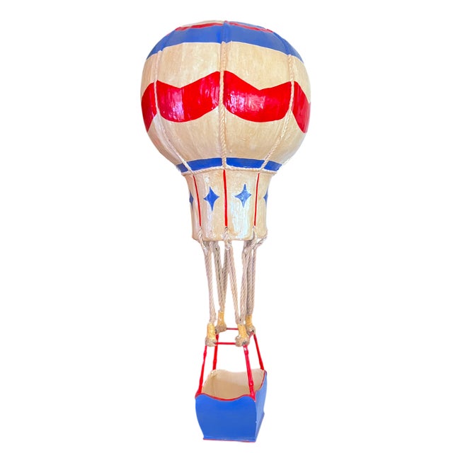 A poetic and sculptural hot air balloon, handcrafted in papier-mâché with hand-painted detailing and rope rigging, evoking...
