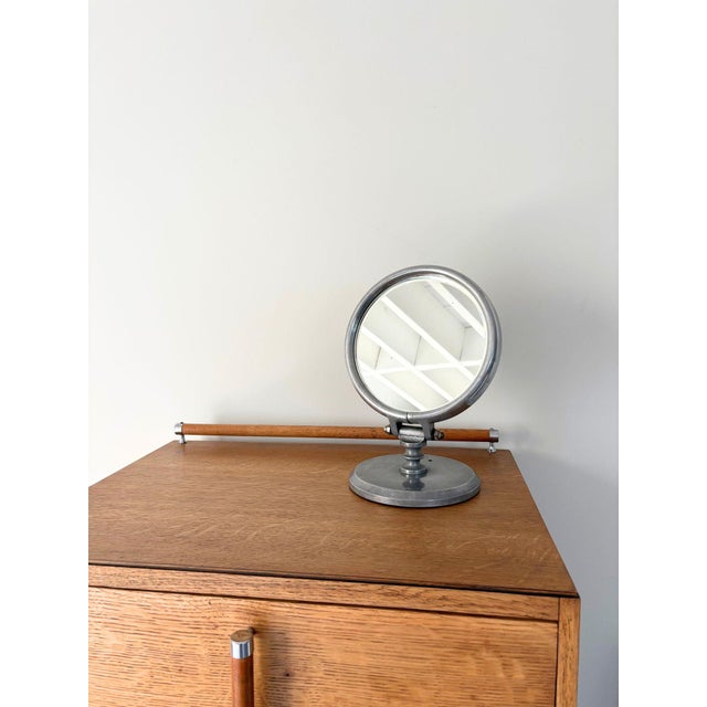 A vintage industrial table top mirror with an art deco aesthetic. This cast metal vanity mirror features a circular glass...