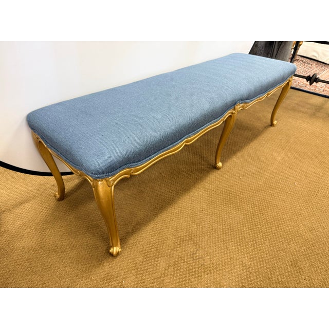 An elegant long upholstered bench with a carved giltwood frame, cabriole legs, and blue textured upholstery. Perfect as a...