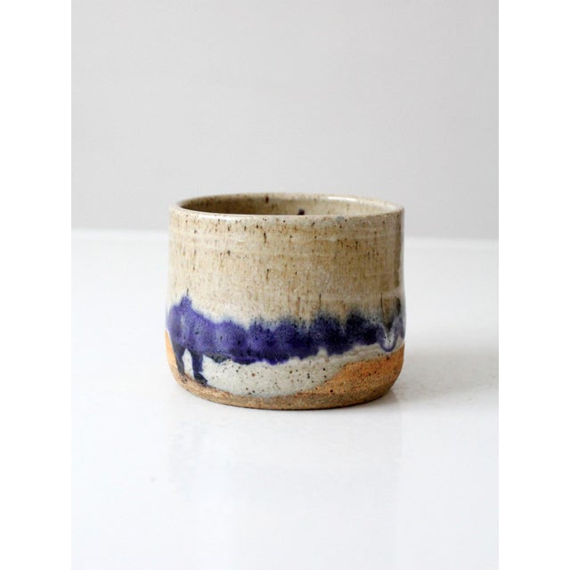 A vintage handmade studio pottery cachepot with a softly cylindrical form and a layered glaze in cream, sand, and deep...