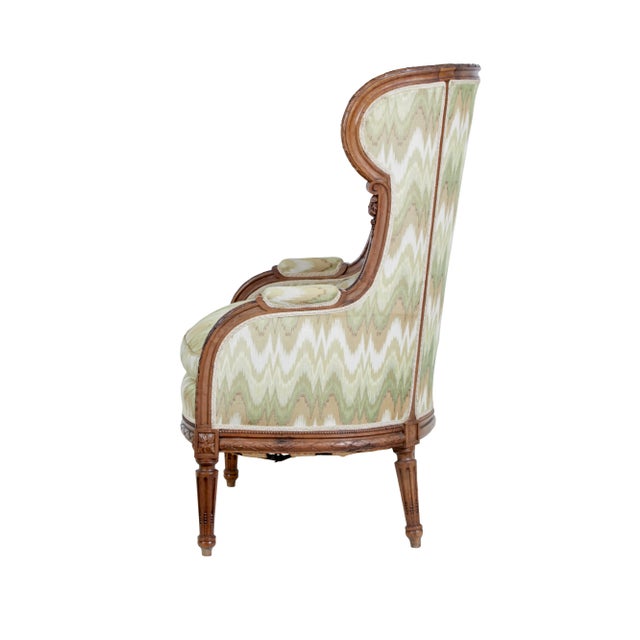 A French Louis XVI style walnut bergère à oreilles circa 1870 with carved décor and fluted legs. Transport yourself to the...