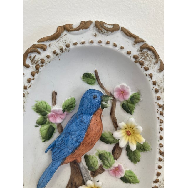 A delightful vintage porcelain wall plaque featuring a raised relief bird perched among flowering branches. The sculptural...