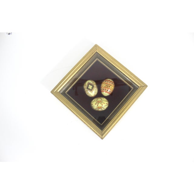 Small framed collection of three hand painted Ukrainian eggs. The frame is painted gold and the backing is a burgundy...