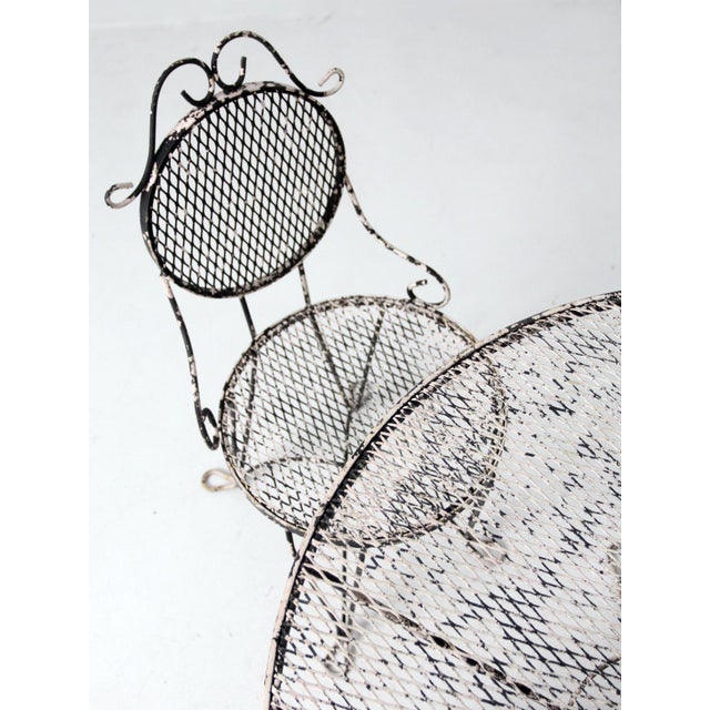 Classic French-inspired iron patio set, featuring a round dining table and four mesh chairs with elegant scrollwork. The...