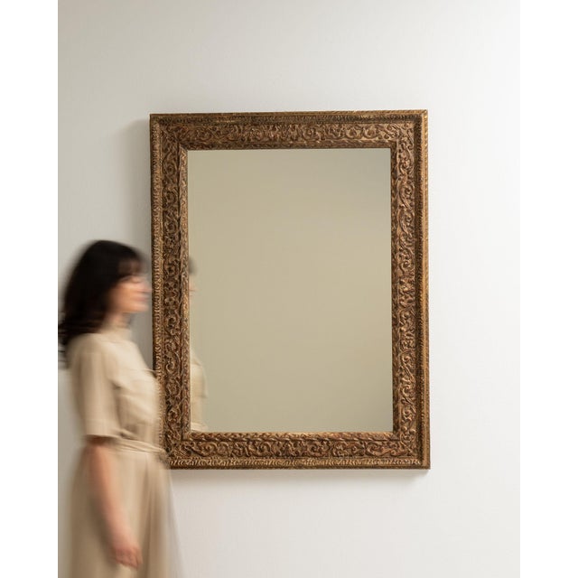Carved giltwood mirror in Antique Gold. Its antique gold finish sets off repeating foliate relief carving around the...