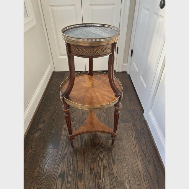 Elegant vintage - mid 20th Century French Louis XVI–style bouillotte table featuring a circular grey marble top set within...